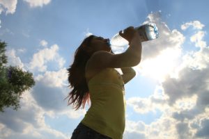 Ragazza all'aperto che beve acqua direttamente dalla bottiglia dopo aver fatto attività fisica.