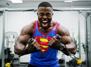 Body-builder in palestra che svolge un esercizio di trazione ai cavi indossando una canotta con lo stemma di superman.