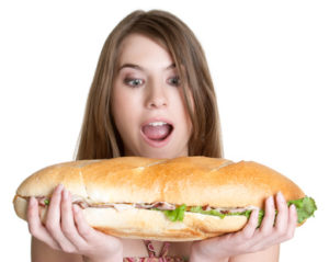 Una ragazza tiene tra le due mani un panino gigante e lo guarda con stupore.