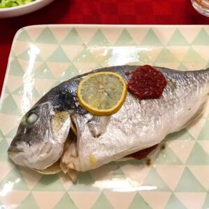 Foto della Ricetta Light della Orata al Cartoccio, impiattata con una fettina di limone e insaporita con del pomodoro secco